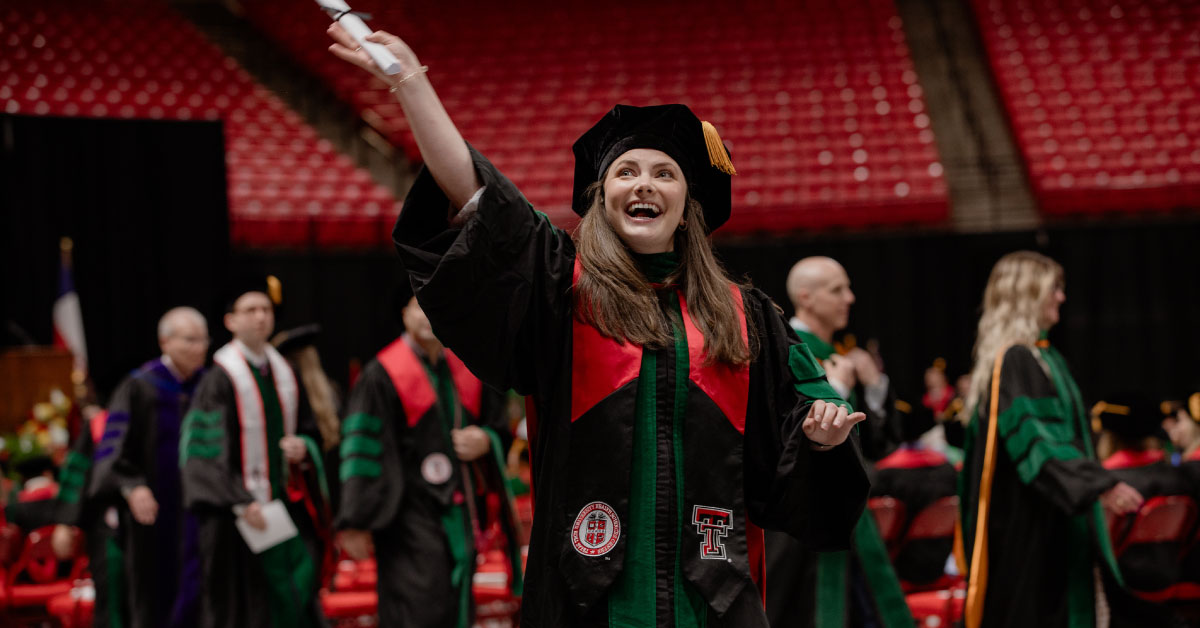 Female TTUHSC medical student wears her graduation cap and gown and holds up her diploma.