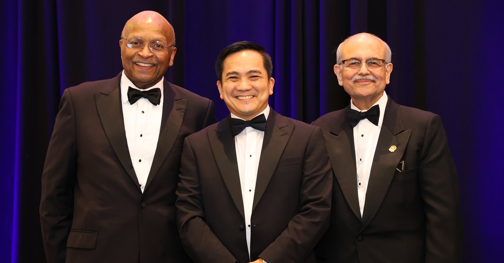 three men standing in suits, smiling