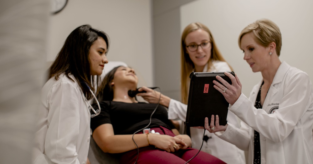 three health care professionals helping a patient who is lying on an exam table 