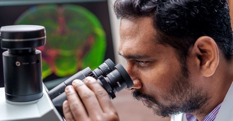 scientist in laboratory looking through a microscope