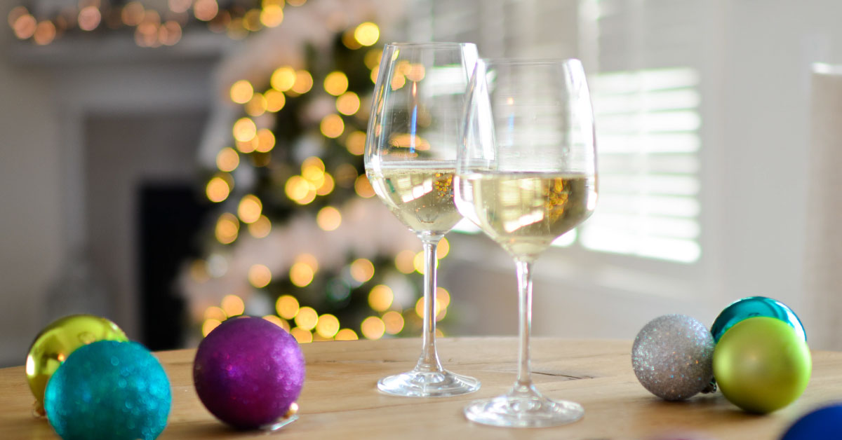 Two glasses of white wine sitting on a table with a Christmas tree in the background.