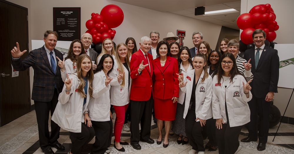 group photo of people in white coats holding up "guns up" signs in celebration of a program naming ceremony