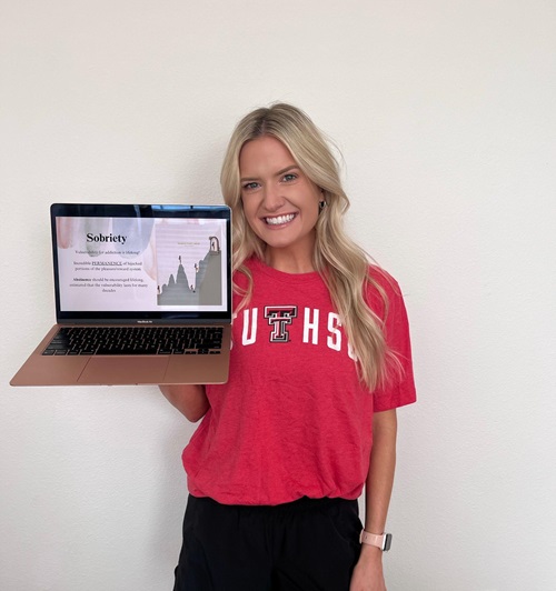woman in TTUHSC t-shirt holding a laptop displaying a presentation on sobriety