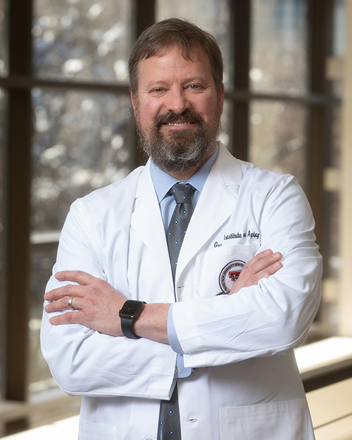 Man wears white coat and stands with his arms crossed.