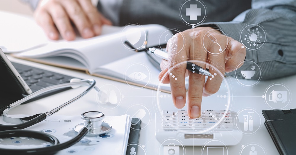 close up photo of hands working with a calculator, with a notebook and stethoscope beside it