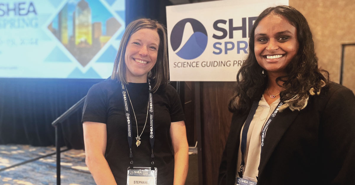 Two woman stand together at a conference and smile.